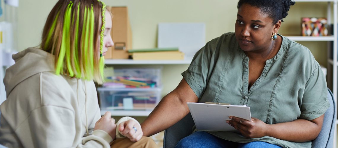African female school psychologist supporting sad teenage girl during her difficult situation at school